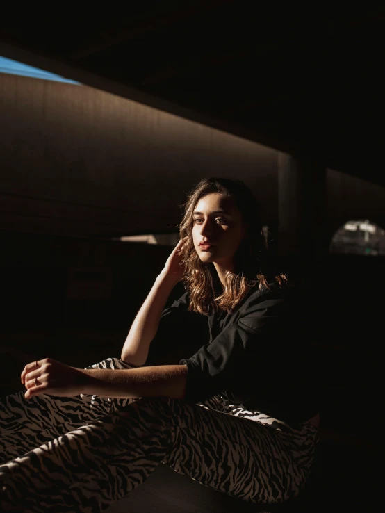 a woman sitting on a bed in the dark, inspired by Elsa Bleda, happening, in the sun, thoughtful pose, portrait photo of a backdrop, low quality photo