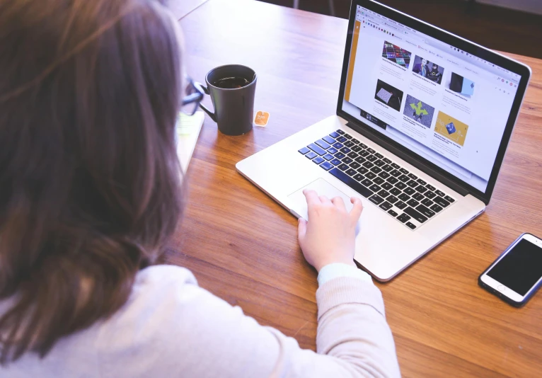 a woman sitting at a table using a laptop computer, a cartoon, trending on unsplash, background image, 9 9 designs, closeup photograph, high angle shot