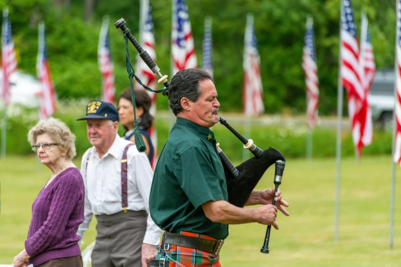a man in a kilt playing a bagpipe, by Scott M. Fischer, pexels contest winner, fourth of july, group photo, green flags, smooth in the background