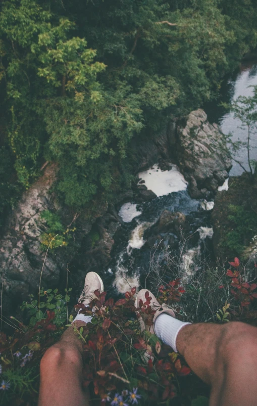 a man sitting on top of a lush green hillside next to a river, by Jessie Algie, pexels contest winner, sneaker photo, head straight down, mid fall, rapids
