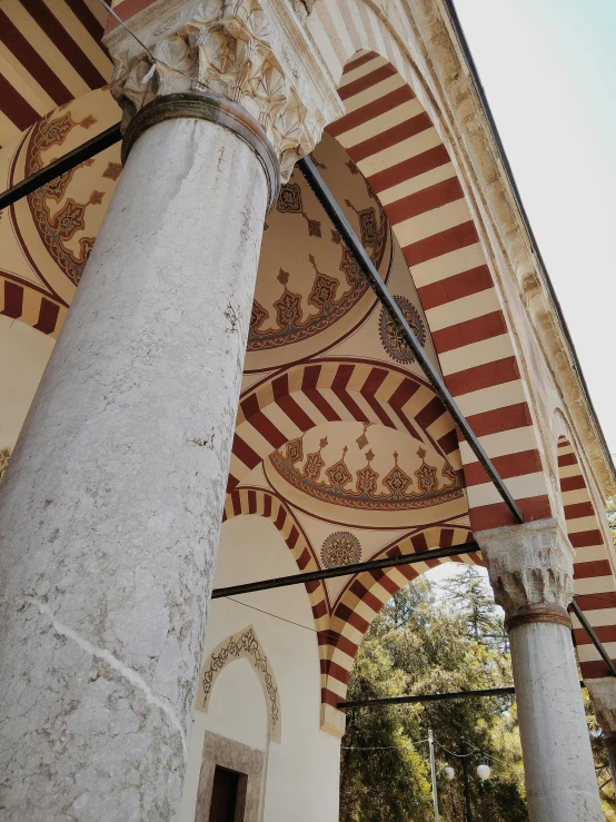 a close up of a building with columns and arches, a mosaic, inspired by Osman Hamdi Bey, unsplash, white buildings with red roofs, low quality photo, photo on iphone, botanical garden