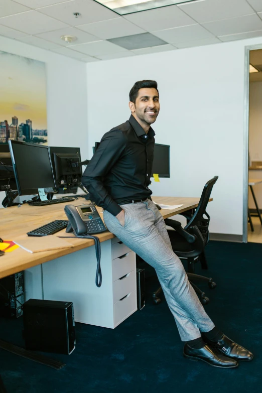 a man sitting on a desk in an office, by Reuben Nakian, trending on reddit, happening, standing athletic pose, smiling, reza afshar, engineering bay