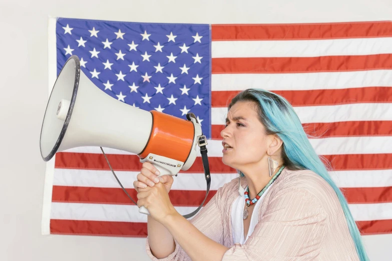 a woman with blue hair holding a megaphone in front of an american flag, unsplash, politicians, 🚿🗝📝