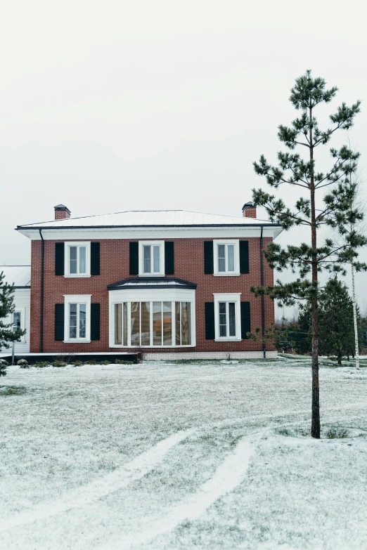 a large house sitting on top of a snow covered field, a colorized photo, inspired by Stanislav Zhukovsky, unsplash, renaissance, front elevation view, brick, pine, overcast day