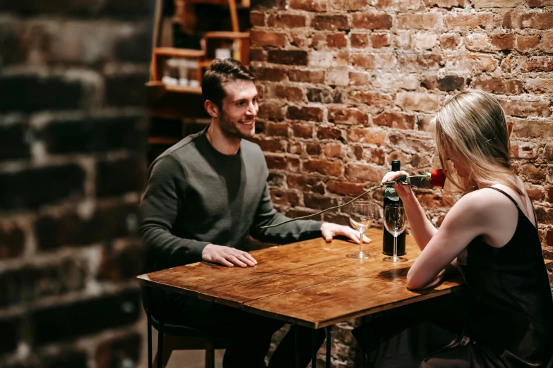 a man and a woman sitting at a table, pexels contest winner, holding wine bottle, closed limbo room, lachlan bailey, looking to his left