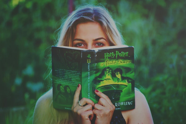 a woman holding a book in front of her face, by Fuller Potter, pexels contest winner, magic realism, harry potter movie screenshot, glowing green, dirty harry potter, ( 3 1