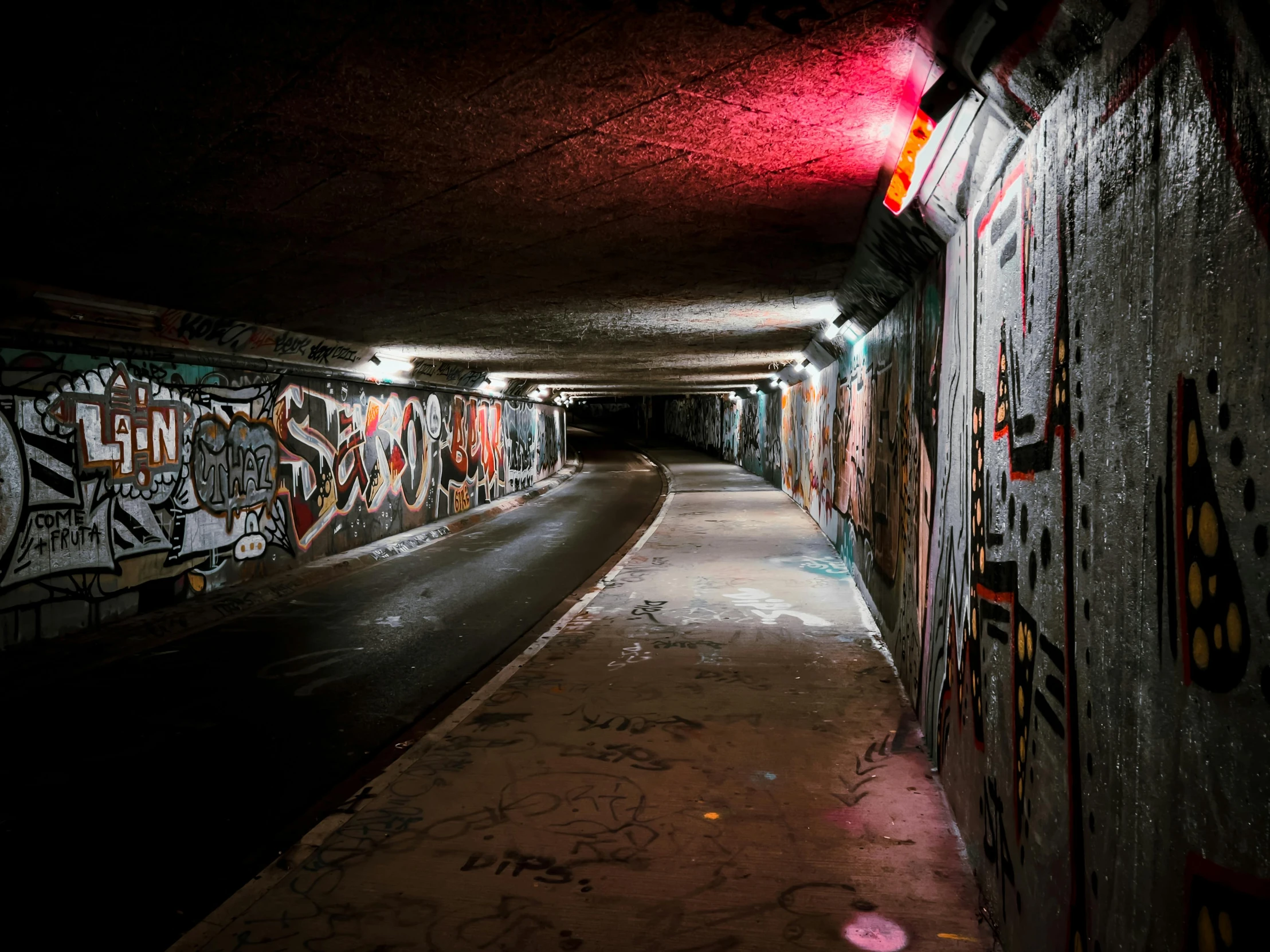 a dark tunnel with graffiti on the walls, colourful lighting, grey, paths, low-light photograph