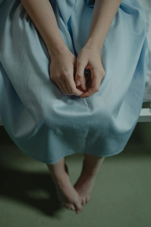 a woman in a blue dress sitting on a bed, unclipped fingernails, at the hospital in patient gown, moody feel, lena oxton