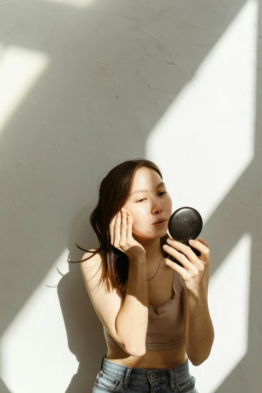 a woman holding a black object up to her face, by Shang Xi, trending on pexels, soft sun lights, with a mirror, skincare, korean woman