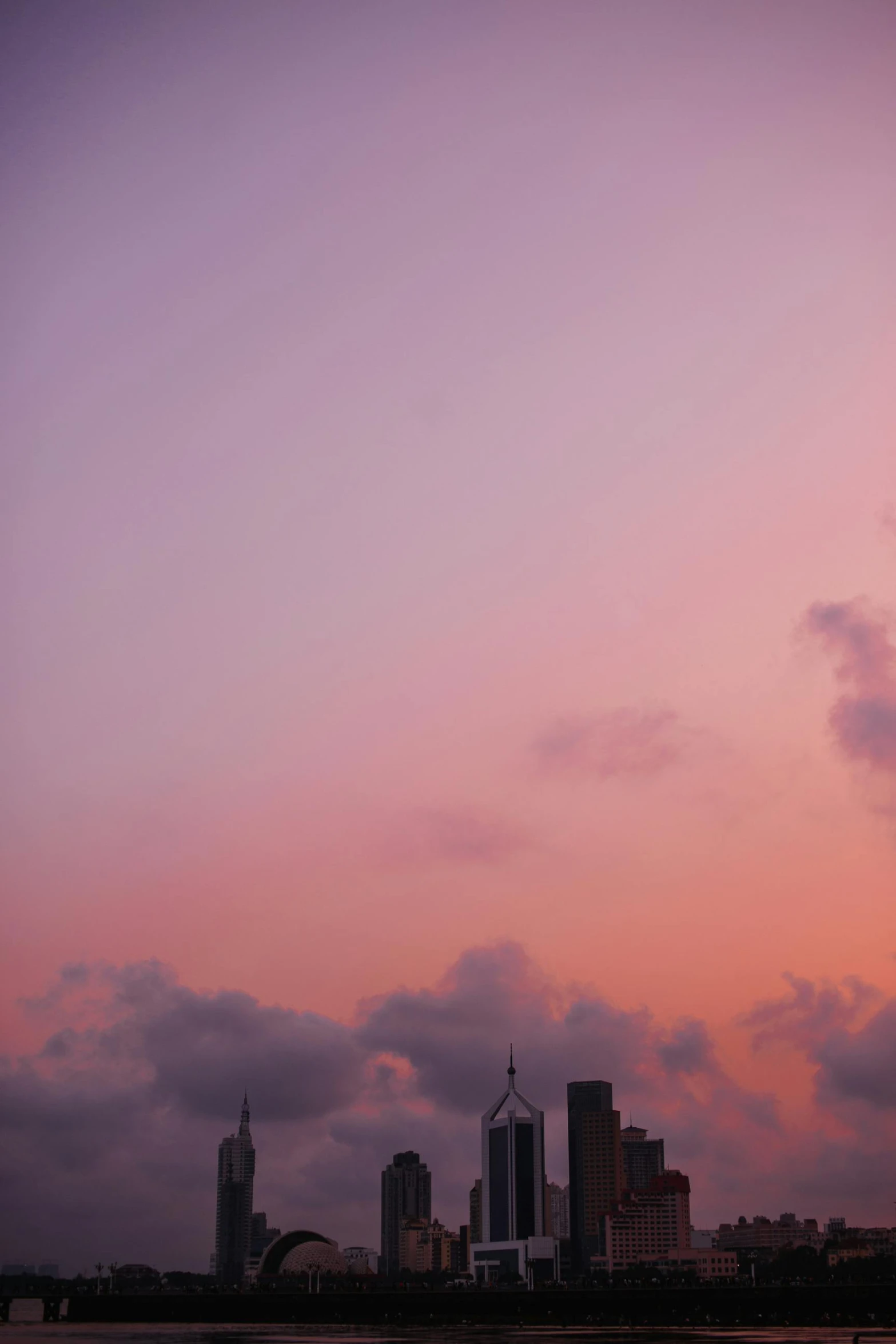 a large body of water with a city in the background, a picture, unsplash, minimalism, pink sunset hue, colombo sri lanka cityscape, three masts, low quality photo