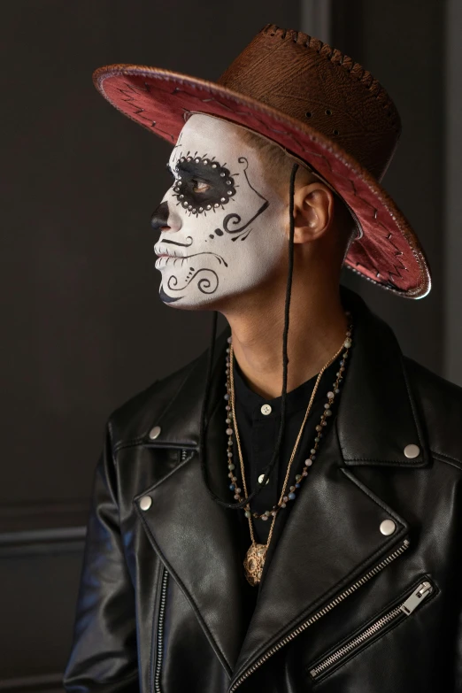 a man with a skull face painted on his face, an album cover, inspired by Byron Galvez, trending on pexels, lowbrow, with hat, lgbtq, mario testino, leather clothing