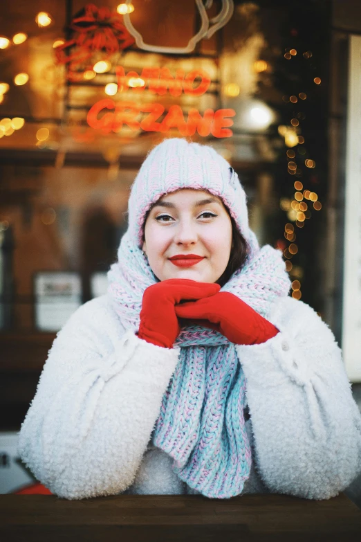 a woman sitting at a table with a cup of coffee, a portrait, by Julia Pishtar, pexels, knitted hat, red gloves, standing in a city center, gif