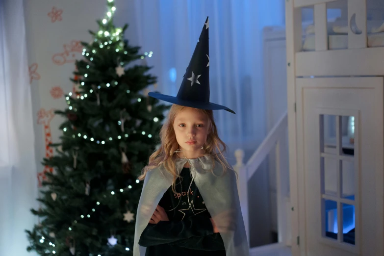 a little girl dressed as a witch standing in front of a christmas tree, pexels, blue wizard hat, ( ( theatrical ) ), fairy lights, in hogwarts