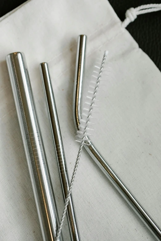 a couple of metal straws sitting on top of a white bag, a still life, unsplash, liquid polished metal, 3 - piece, eco, metal tail