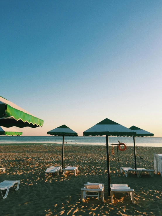 a number of lawn chairs and umbrellas on a beach, an album cover, unsplash, renaissance, black sea, profile image, golden hour photo, #green