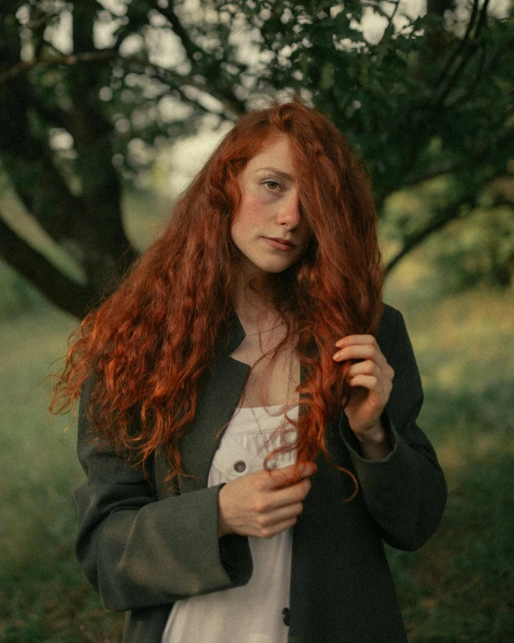 a woman with long red hair standing under a tree, inspired by Elsa Bleda, trending on pexels, renaissance, androgynous male, curly haired, she wears a jacket, ((portrait))