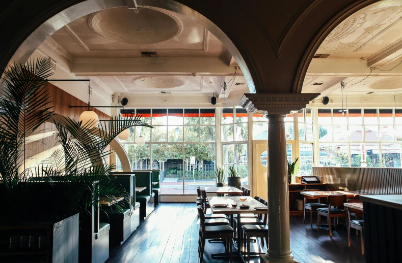 a dining room filled with lots of tables and chairs, inspired by Richmond Barthé, unsplash, art nouveau, palm trees outside the windows, caulfield, mezzanine, warm natural lighting