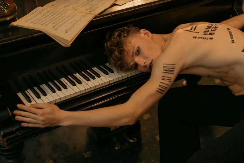 a shirtless man laying on top of a piano, trending on pexels, bauhaus, beautiful androgynous prince, tattoos all over the skin, non-binary, promotional image