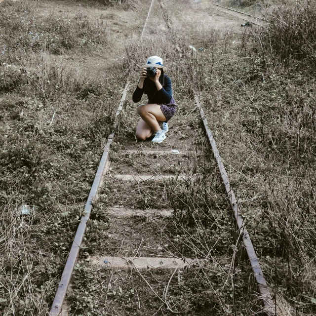 a woman kneeling on a train track taking a picture, dilapidated look, 5 feet distance from the camera, high angle camera, julia sarda