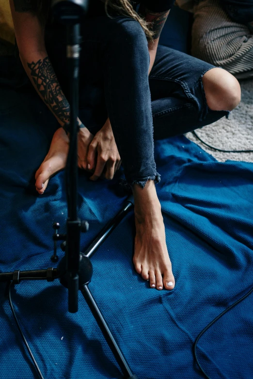 a man sitting on top of a bed next to a camera, a tattoo, by Elsa Bleda, trending on pexels, navy blue carpet, bassist, detailed foot shot, flirting