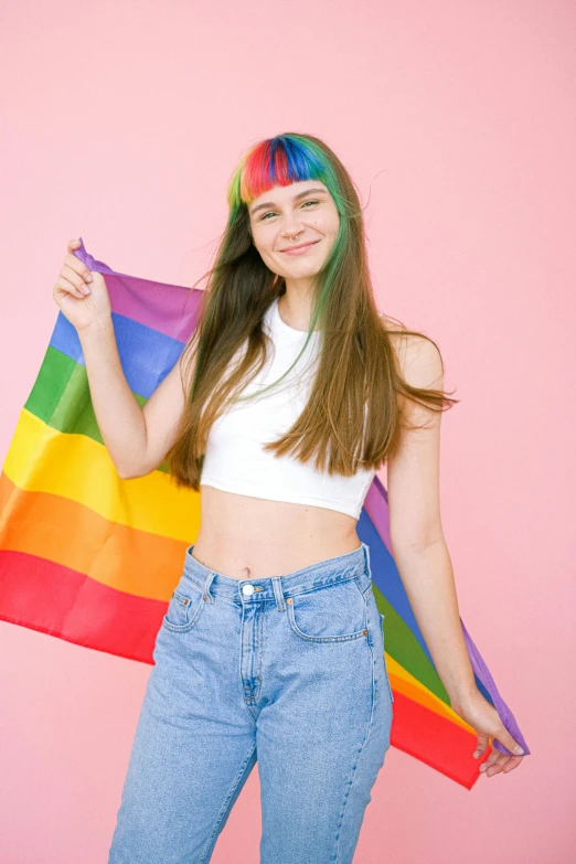 a young woman holding a rainbow flag against a pink background, by Julia Pishtar, trending on pexels, straight bangs, wearing a crop top, on white background, 19-year-old girl
