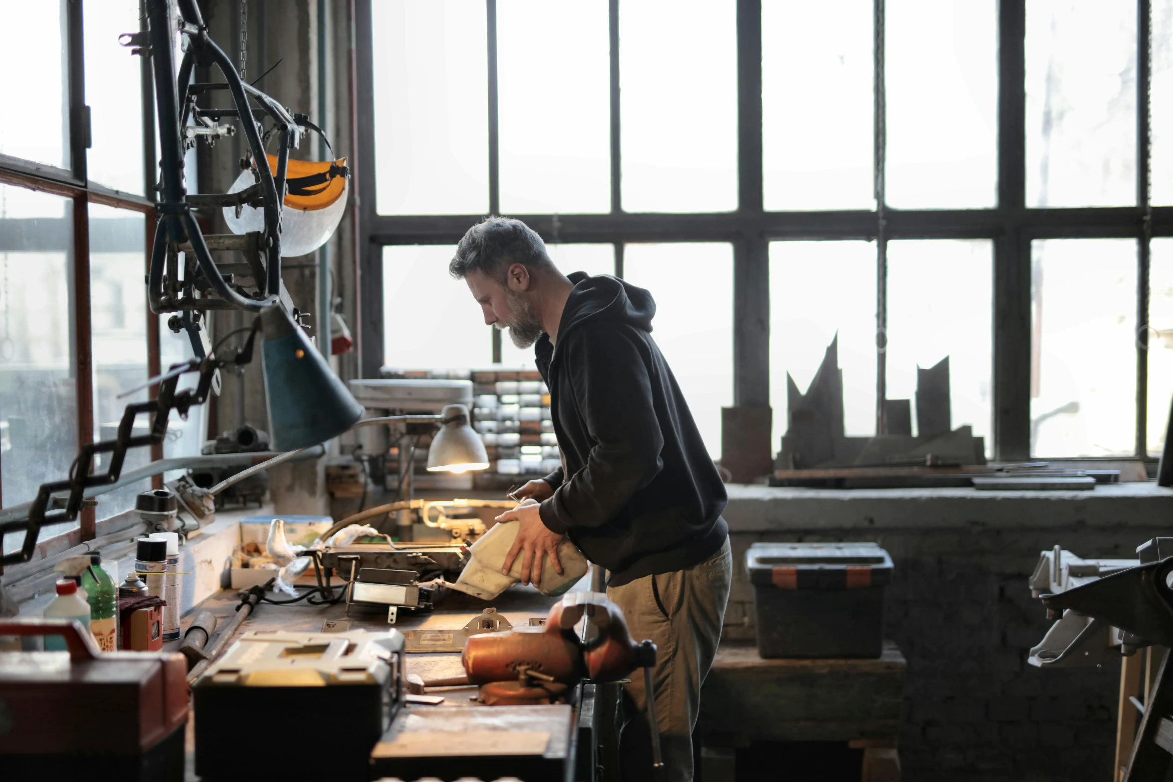 a man that is standing in front of a table, pexels contest winner, arbeitsrat für kunst, scrap metal on workbenches, working on a laptop at a desk, vermeer lighting, sydney hanson