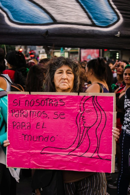 a woman holding a sign in front of a crowd, an album cover, by Alejandro Obregón, trending on unsplash, feminist art, older woman, maternal, mexican, 15081959 21121991 01012000 4k