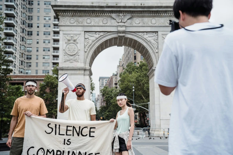 a group of people holding a sign that says silence is compliance, by Nina Hamnett, unsplash, renaissance, nypd, a person standing in front of a, colour film street photography, white ribbon