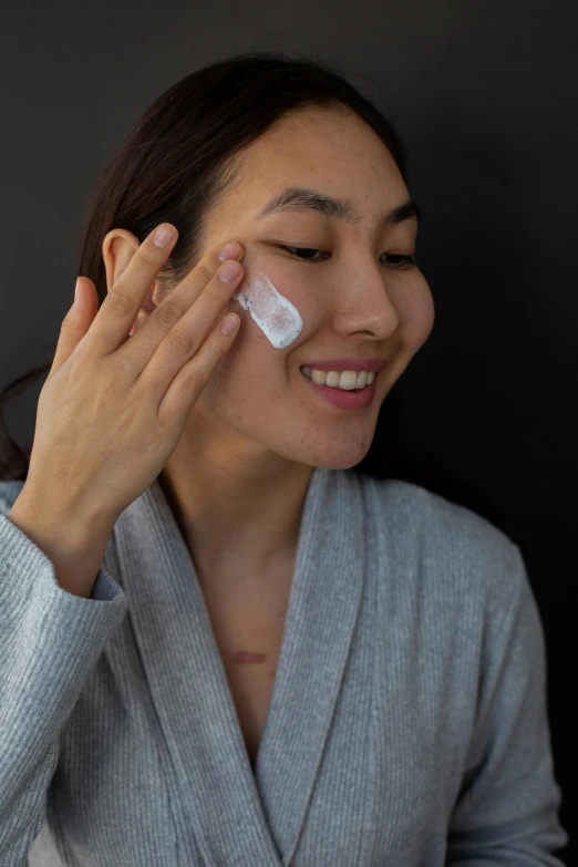 a woman is putting cream on her face, inspired by Li Di, happening, a plaster on her cheek, grey, mobile, japanese collection product