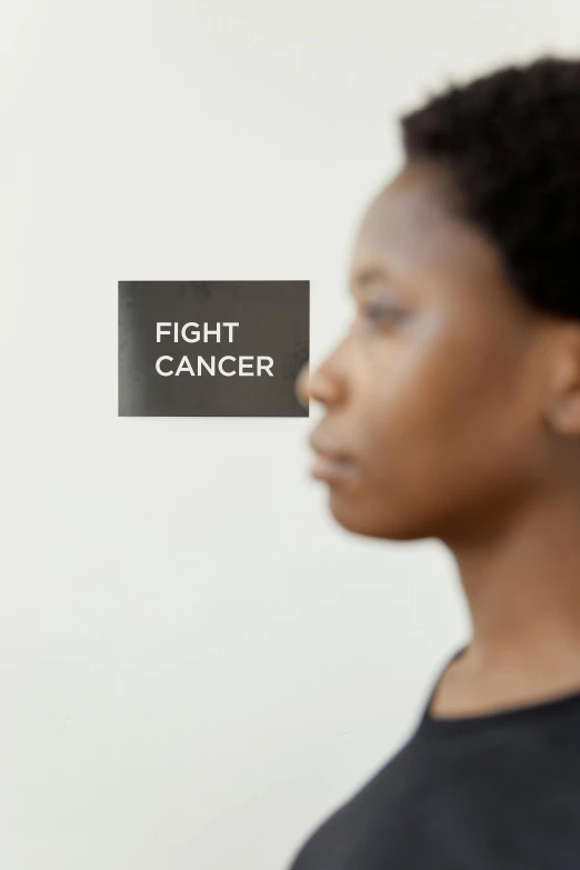 a woman with a sign that says fight cancer, inspired by Gordon Parks, facing sideways, close - up photograph, gray, getty images