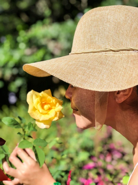 a woman smelling a yellow rose in a garden, by Ellen Gallagher, unsplash, wearing wide sunhat, pith helmet, transparent, closeup - view