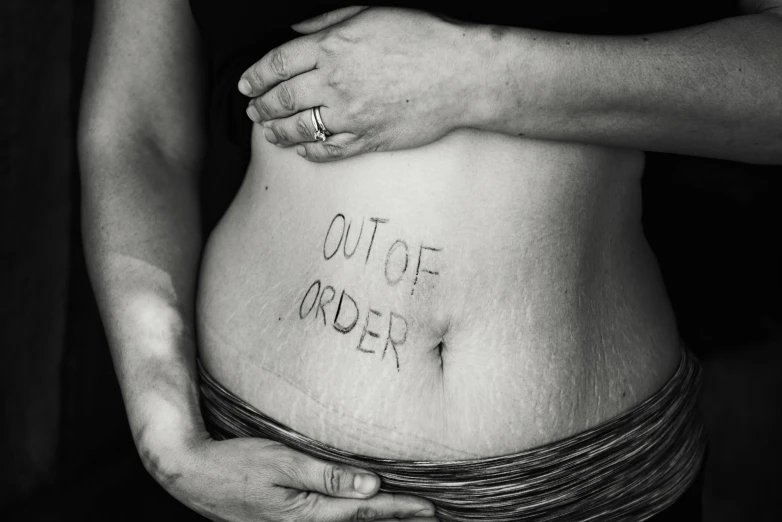 a pregnant belly with the words out of order written on it, by Caro Niederer, skin, photoshoot, trauma, tap out