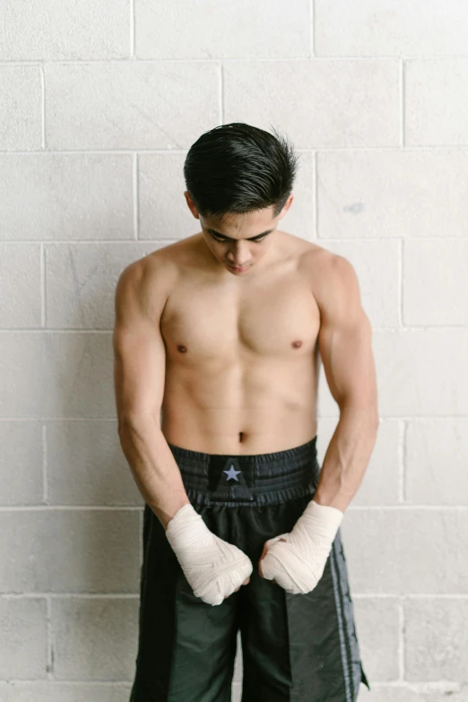 a shirtless man standing in front of a white brick wall, inspired by Randy Vargas, elbow gloves, profile image, fit pic, teenage boy