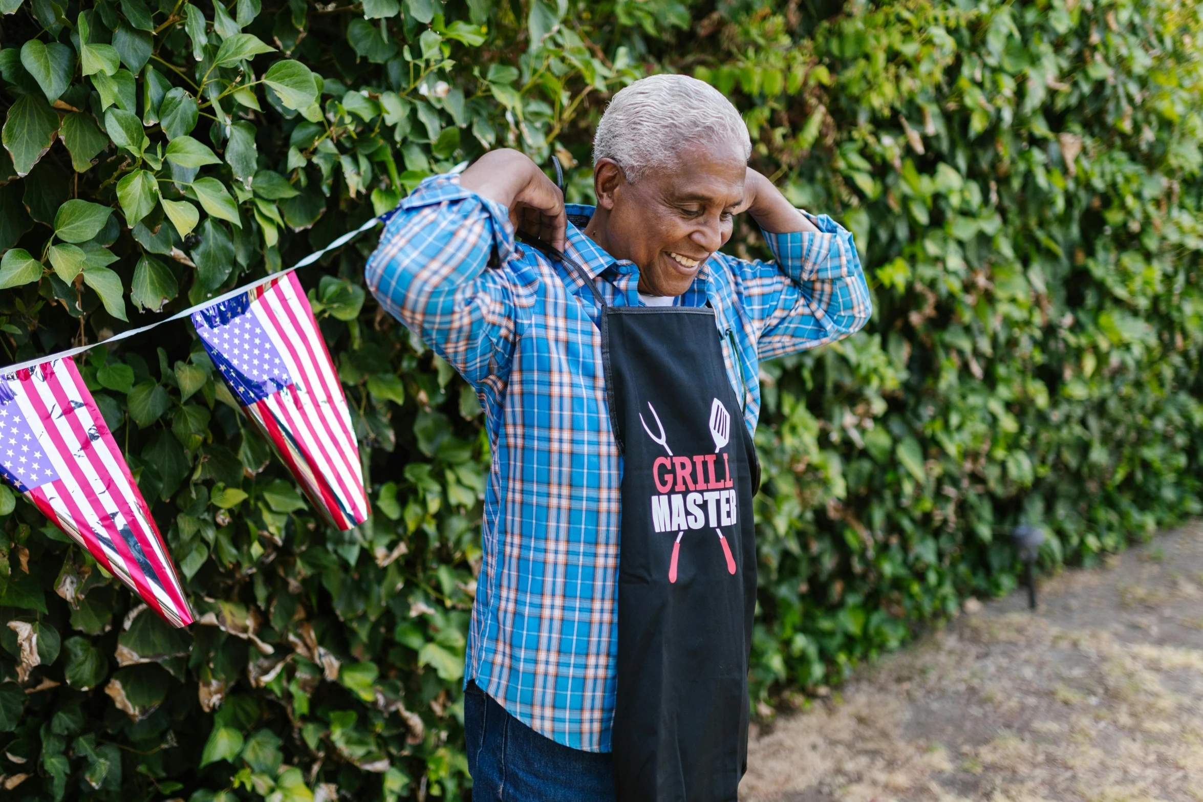 a man standing in front of a hedge holding an american flag, a photo, by Everett Warner, pexels contest winner, black arts movement, ogre chef in an apron, a still of a happy, grand master, dripping bbq sauce