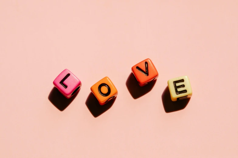 the word love spelled with cubes on a pink background, by Olivia Peguero, trending on pexels, letterism, beads, orange pastel colors, enamel, slides