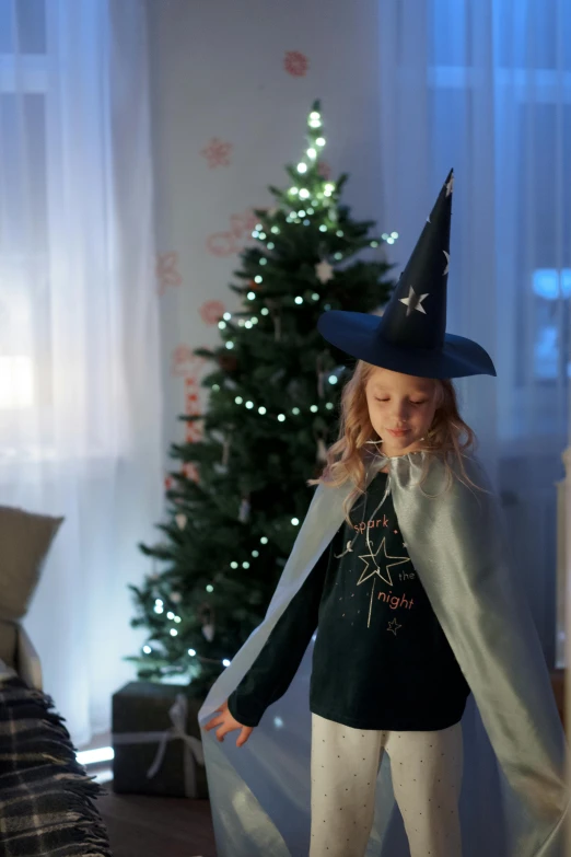 a little girl standing in front of a christmas tree, pexels, magical realism, wearing a grey wizard hat, gif, wearing hero costume, indoor scene