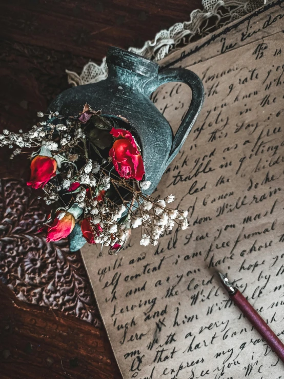 a piece of paper sitting on top of a wooden table, a still life, inspired by Franz von Lenbach, unsplash contest winner, romanticism, small red roses, intricate writing, thumbnail, medieval photograph