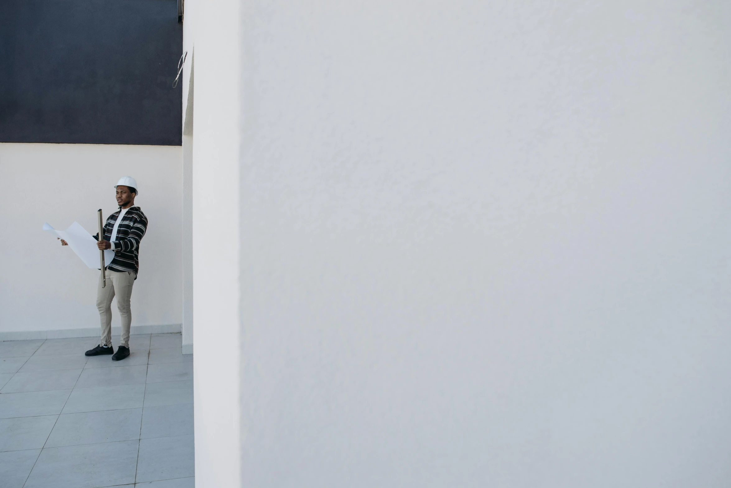 a man standing on a sidewalk holding an umbrella, by Paolo Parente, unsplash, white minimalist architecture, background image, construction, peruvian looking