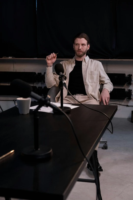 a man sitting at a table in front of a microphone, unsplash, photorealism, theatrical, video still, in a studio, aphex twin