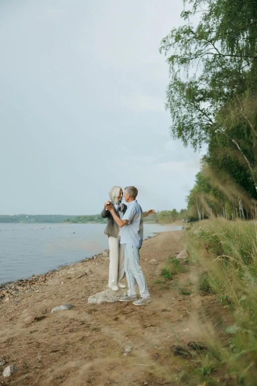 a man and a woman standing on a beach next to a body of water, by Grytė Pintukaitė, couple dancing, lush surroundings, in russia, 15081959 21121991 01012000 4k