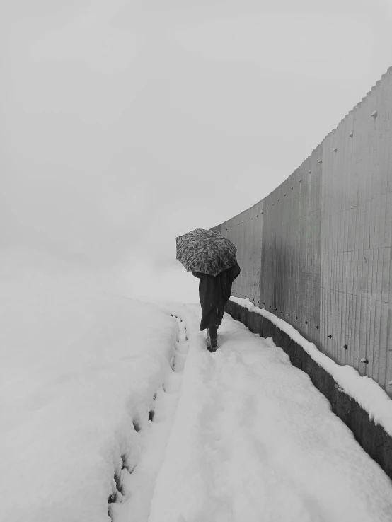 a person walking in the snow with an umbrella, a black and white photo, inspired by Sergio Larraín, conceptual art, fog. by greg rutkowski, reza afshar, wall, carrying big sack