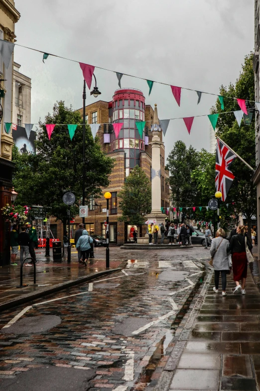 a group of people walking down a wet street, inspired by L. S. Lowry, unsplash, art nouveau, union jack, green square, panoramic shot, clock tower