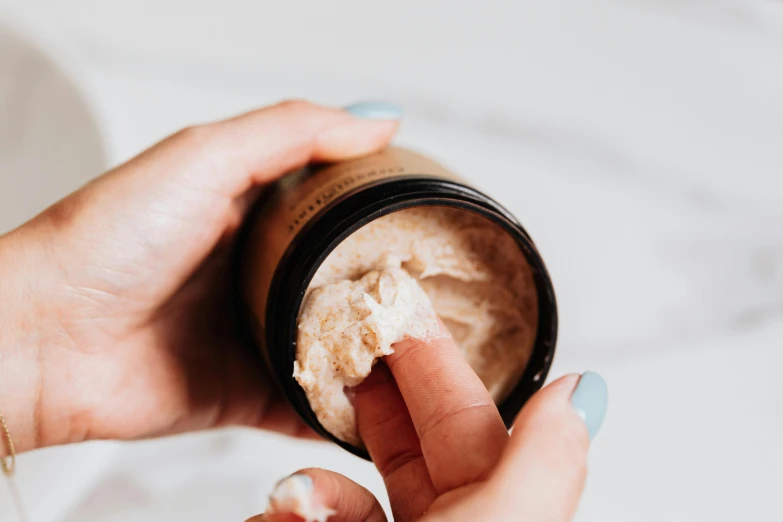 a close up of a person holding a jar of cream, by Emma Andijewska, trending on pexels, textured base ; product photos, tan skin, handcrafted, multi-part