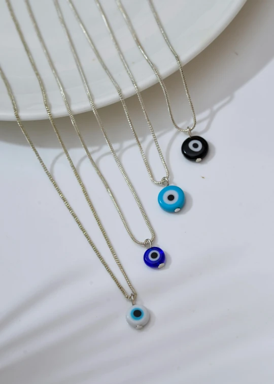 four evil eye necklaces on a white plate, blue silver and black, birdseye view, 🤬 🤮 💕 🎀, middle close up shot