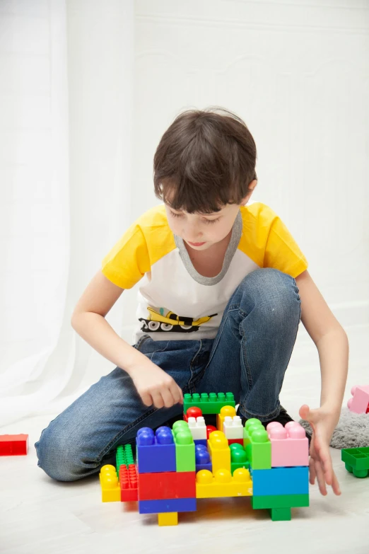 a young boy sitting on the floor playing with legos, inspired by Sam Havadtoy, shutterstock, transgender, square, multi colour, grey