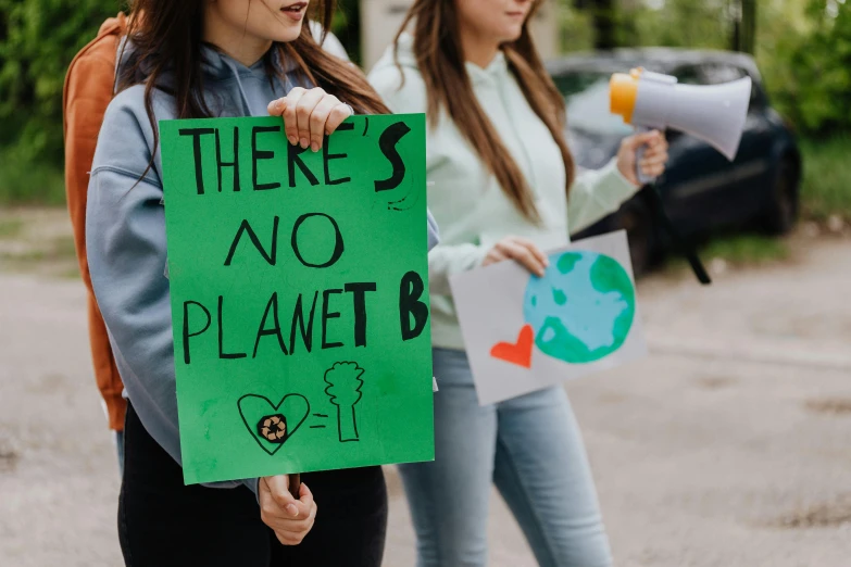 a woman holding a sign that says there's no planet b, trending on pexels, woman holding another woman, green and black, teenage no, biodiversity all round