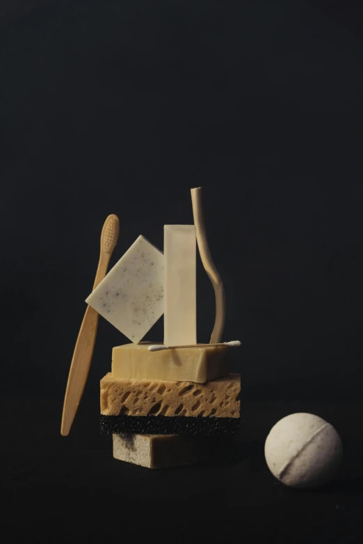 a piece of cheese sitting on top of a table next to a ball, an abstract sculpture, inspired by Isamu Noguchi, conceptual art, ((still life)), soap, cane, alex kanevsky