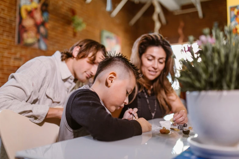 a group of people sitting around a table eating food, a child's drawing, pexels contest winner, husband wife and son, te pae, paint-on-glass painting, looking across the shoulder