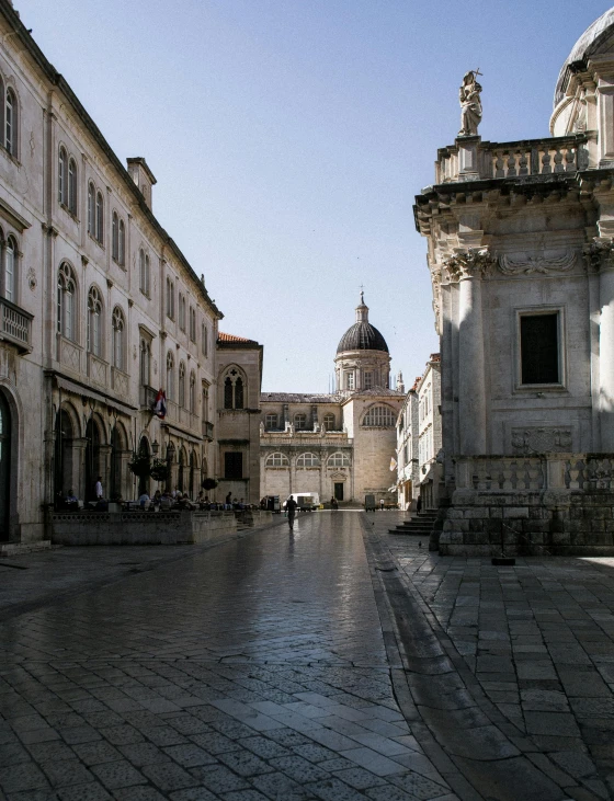 a cobblestone street with a clock tower in the background, by Matija Jama, with great domes and arches, profile image, square, split near the left