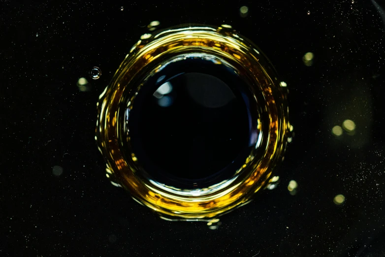 a glass filled with liquid sitting on top of a table, inspired by Otto Piene, unsplash, space art, black circle, ornate galactic gold, high resolution macro photo, olive oil